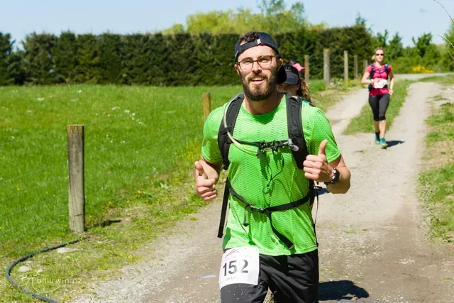 A man with a backpack is running down a dirt road.