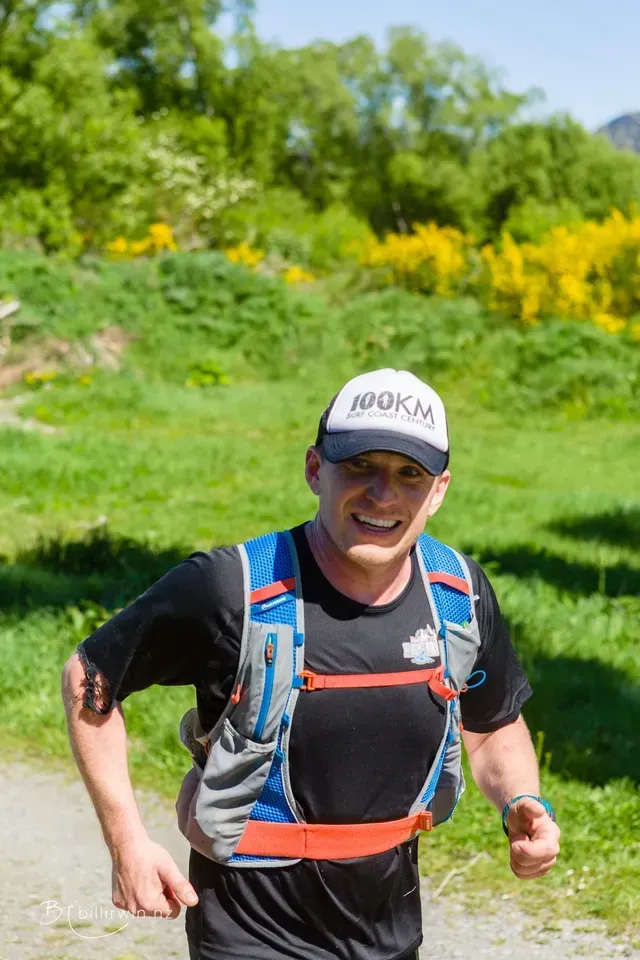 A man wearing a hat and a backpack is running on a trail.