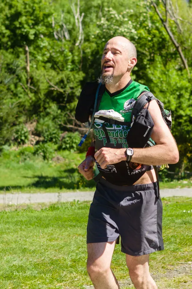 A man is running in a park with a backpack on his back.