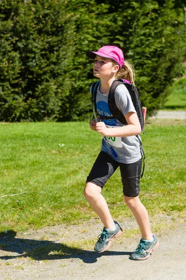 A young girl wearing a pink hat and a backpack is running down a dirt road.