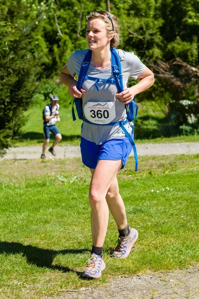 A woman is running in a race with a backpack on her back.