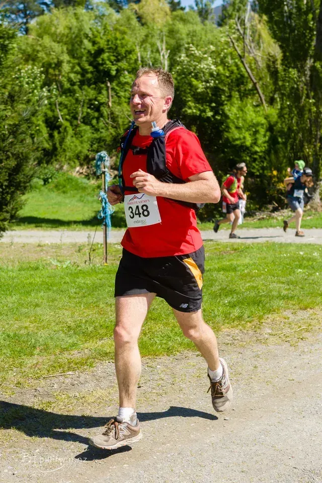 A man in a red shirt and black shorts is running in a park.