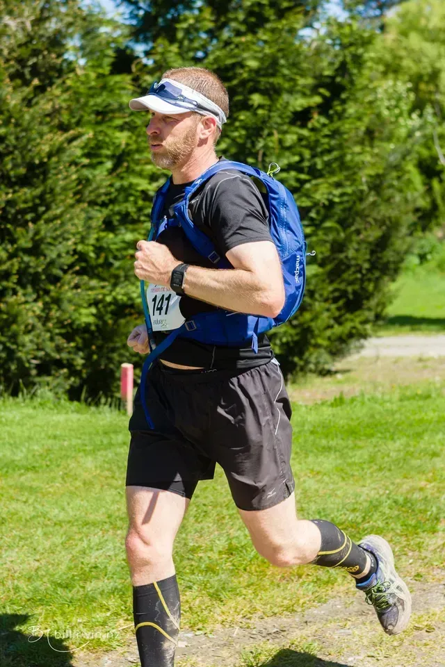 A man is running in a park with a backpack on his back.
