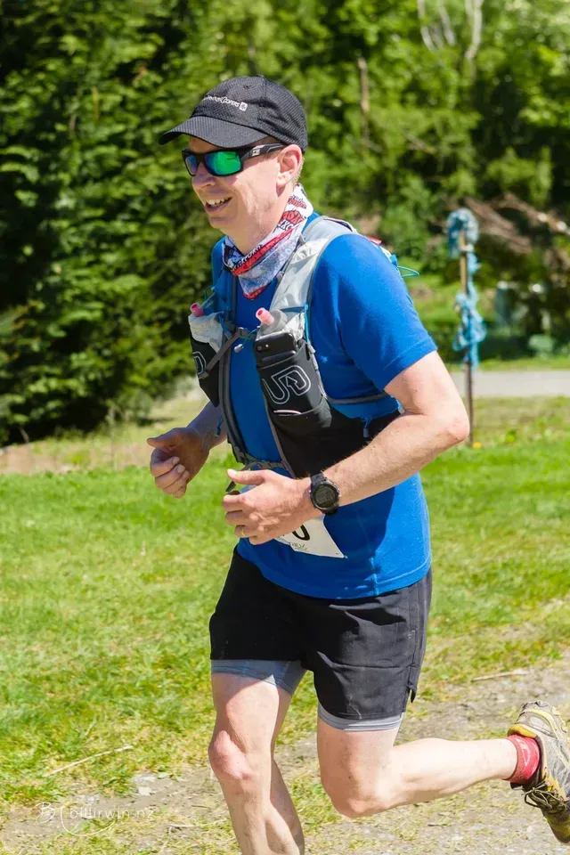 A man in a blue shirt and black shorts is running in a park.