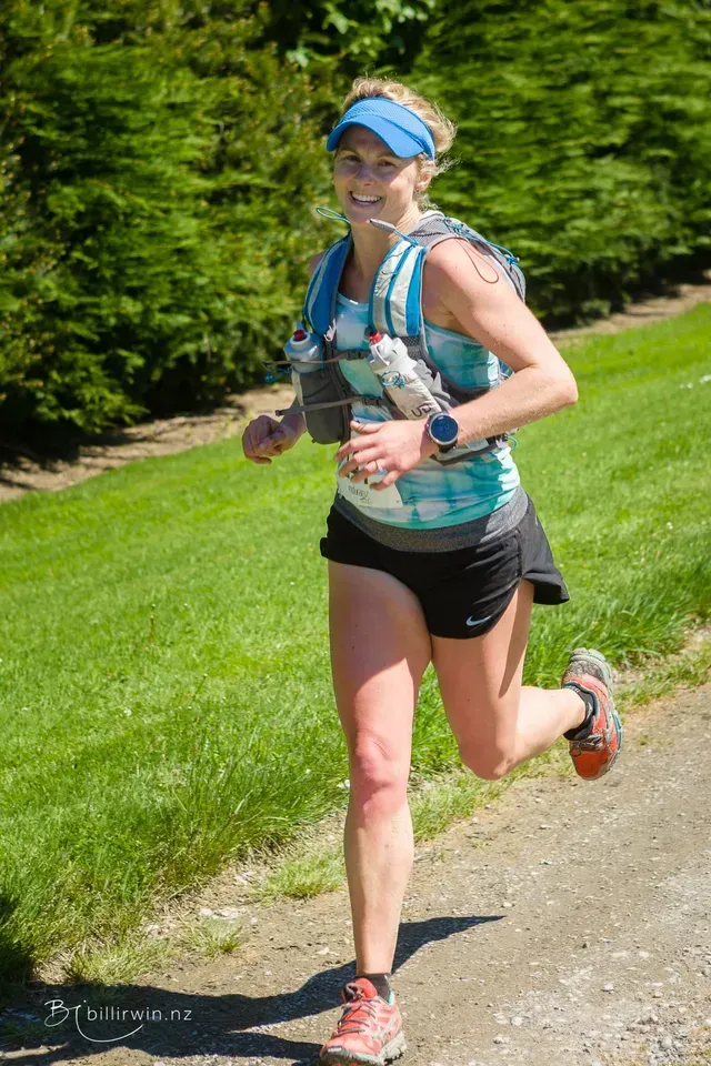 A woman is running down a dirt road with a water bottle in her hand.