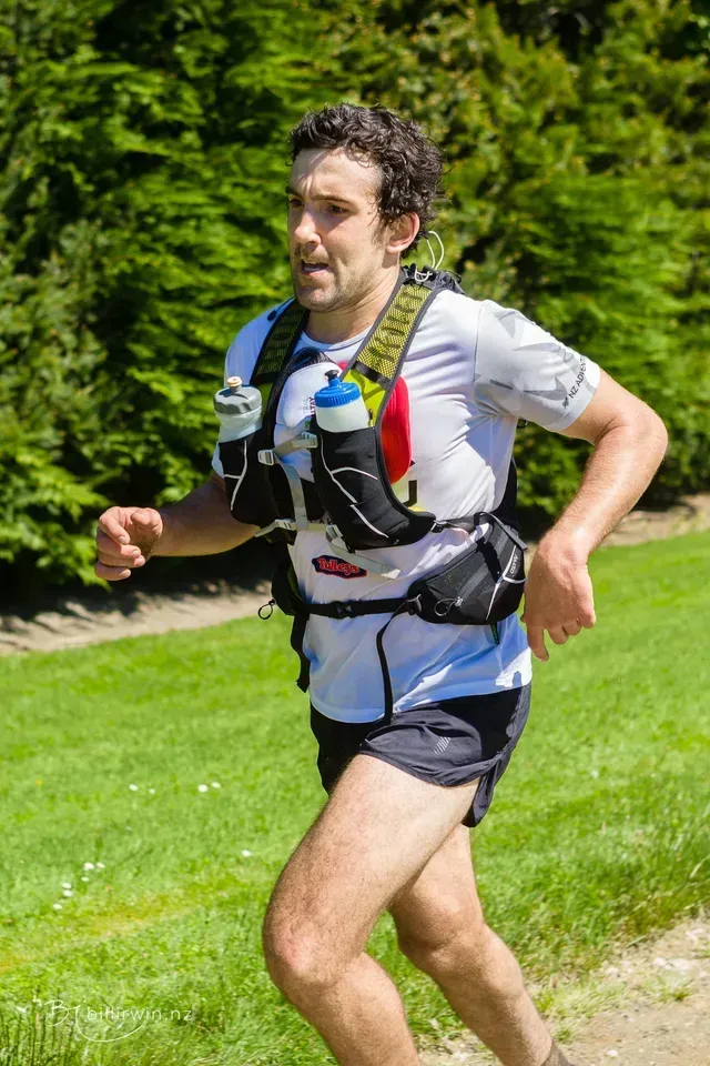 A man is running on a trail with a water bottle in his hand.