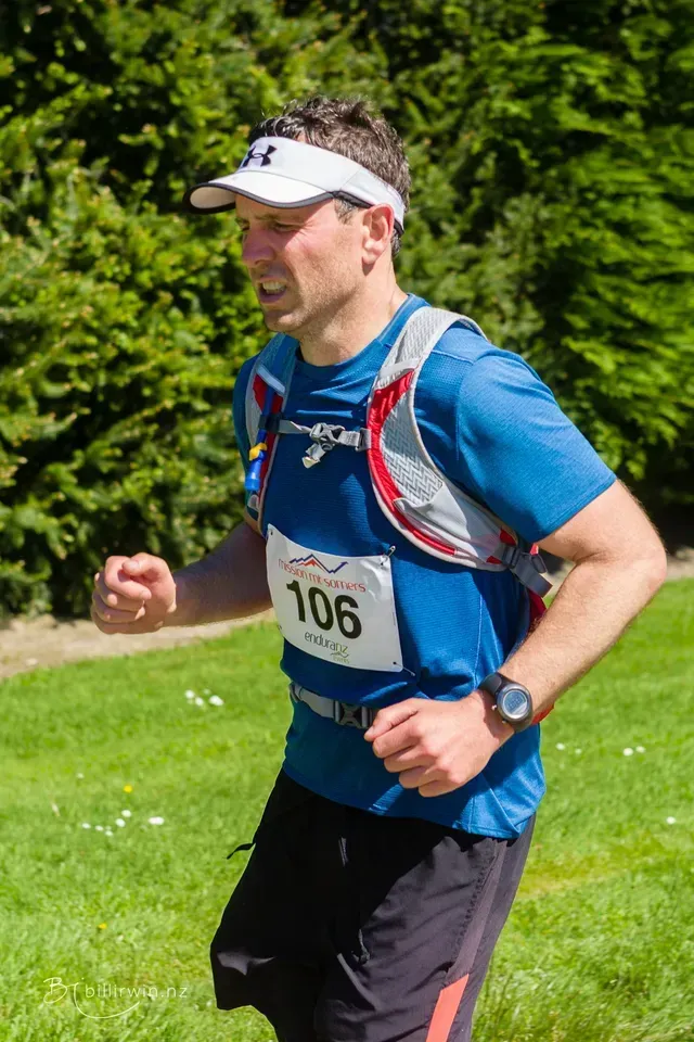 A man wearing a blue shirt and a visor is running in a field.
