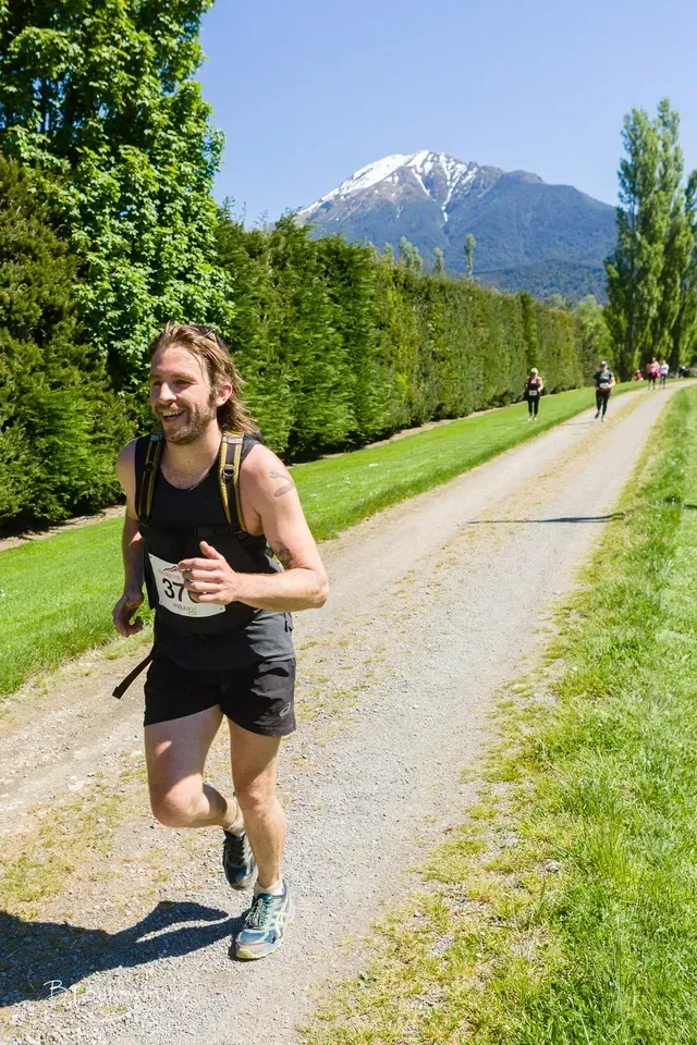 A man is running down a dirt road with a mountain in the background.