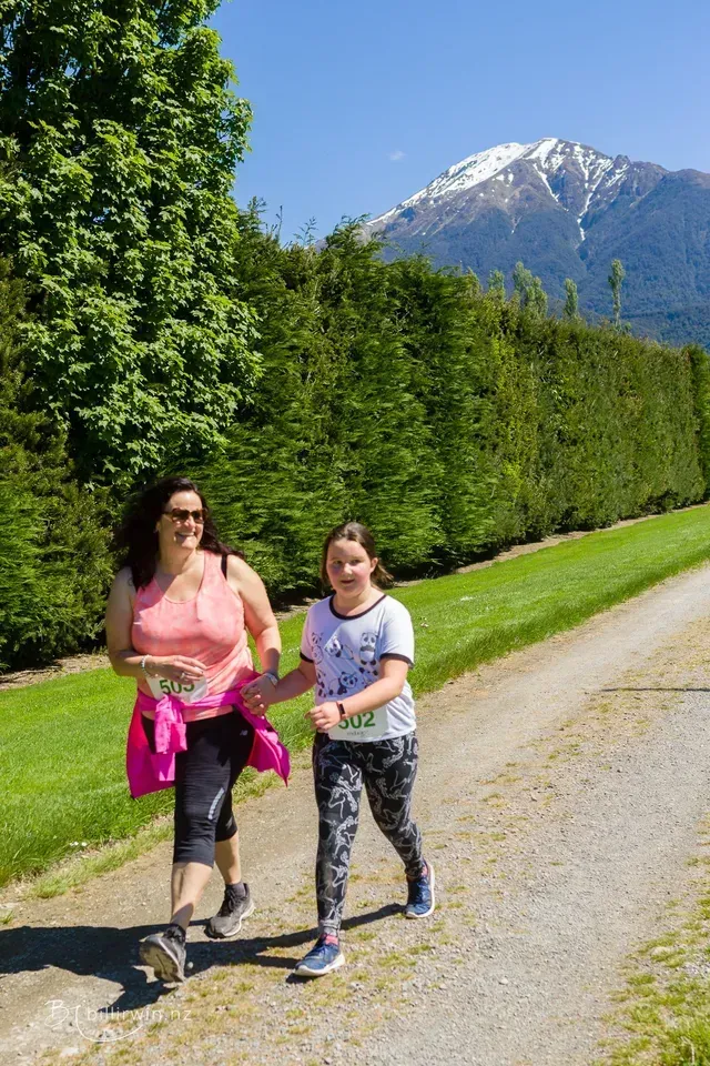 A woman and a girl are walking down a dirt road holding hands.