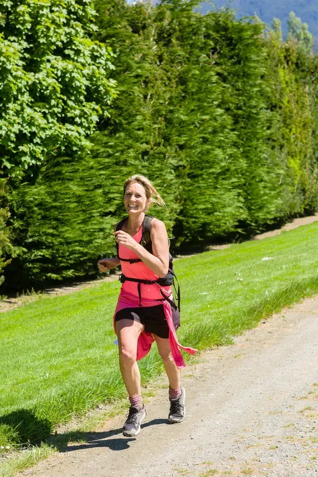 A woman is running down a dirt road in a park.
