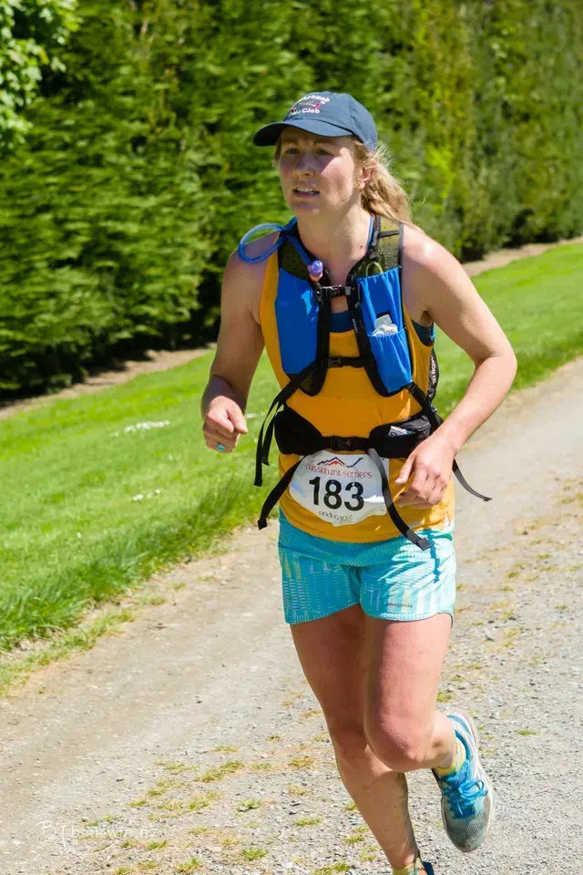 A woman is running down a dirt road wearing a number 183 bib.