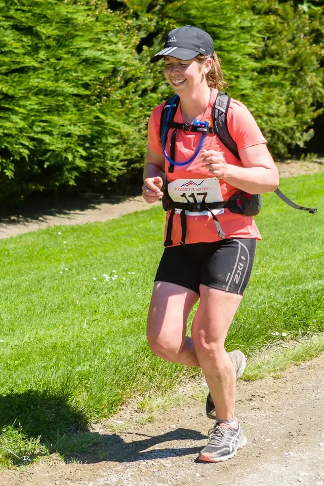A woman with a backpack is running down a dirt road.