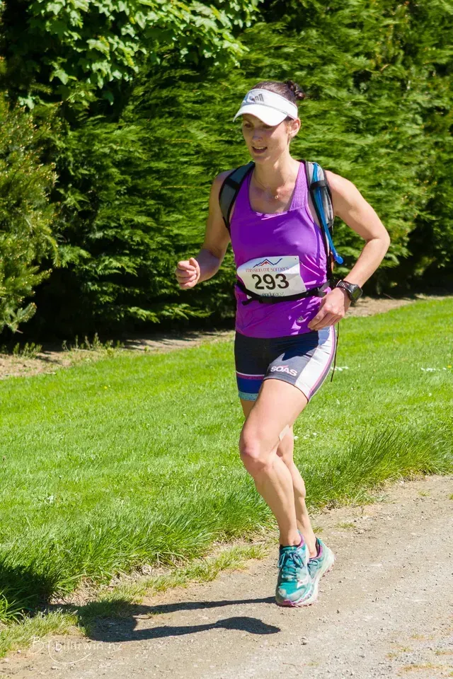 A woman in a purple tank top and shorts is running a race.