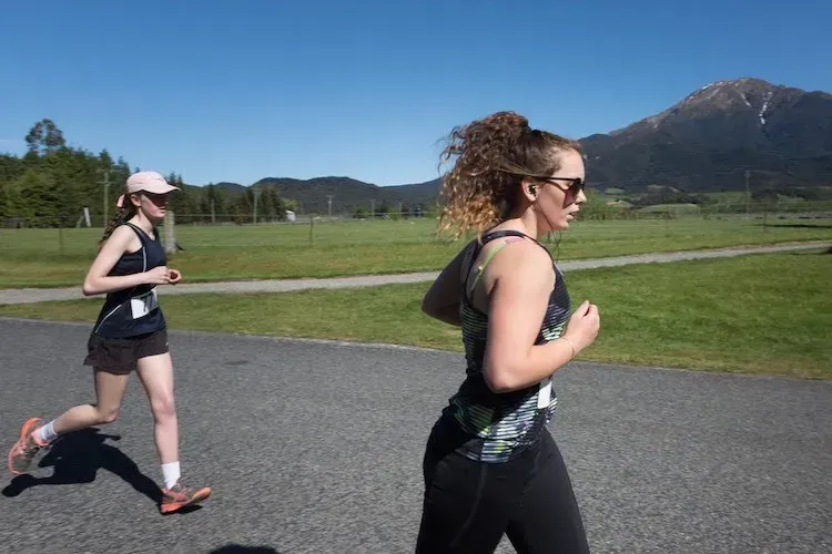 Two women are running on a road with a mountain in the background.