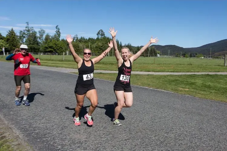 Two female runners are posing for a picture with their arms in the air.