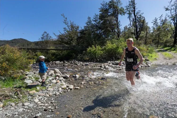 A woman is running through a river while a child watches.