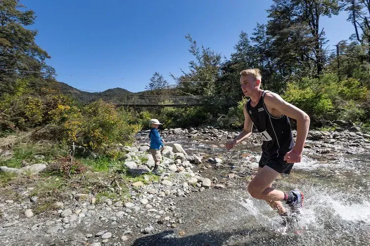 A man is running through a stream in the woods.
