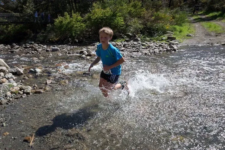 A young boy is running through a stream of water.