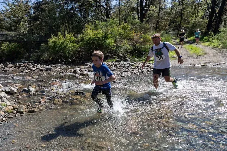 A man and a boy are running through a river.