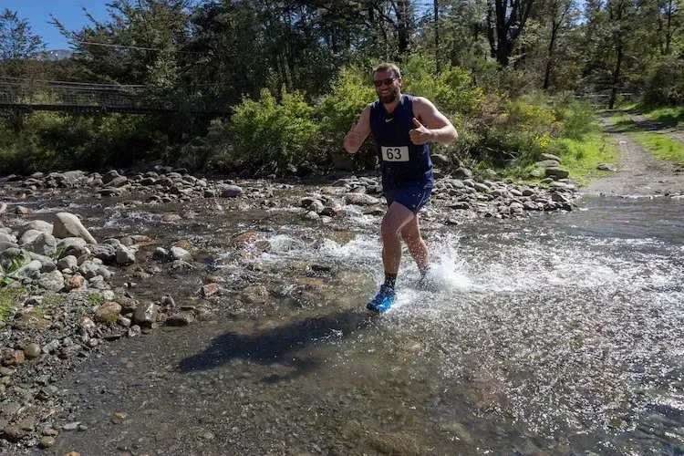 A man in a blue tank top is running through a river.