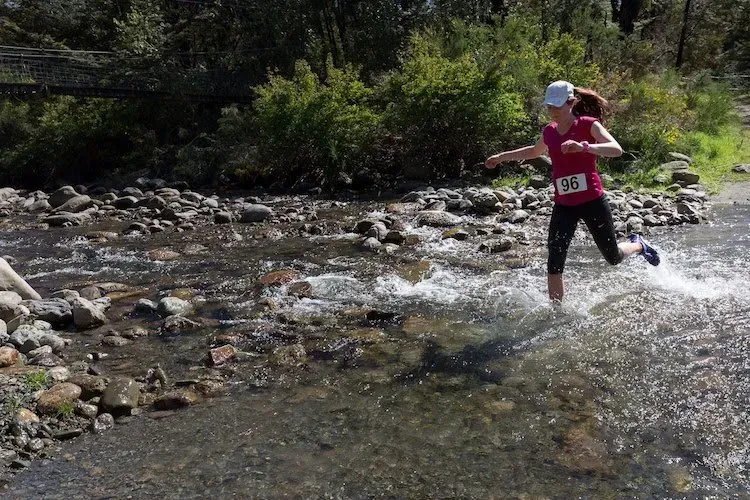 A woman in a red shirt is running through a river