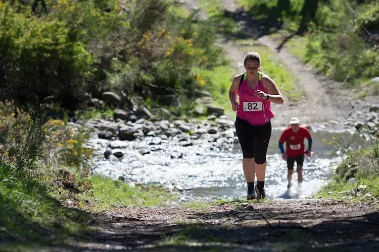 A woman is running on a trail next to a river.