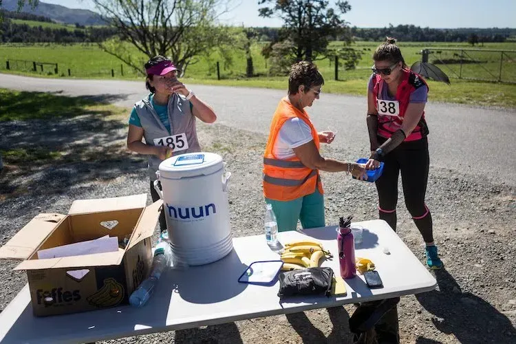 Three women are standing around a table with a bucket that says nuun on it.