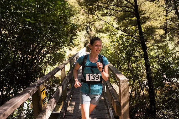 A woman wearing a number 139 shirt is running across a wooden bridge.