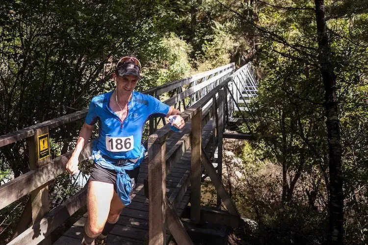A woman in a blue shirt with the number 186 on it is crossing a wooden bridge.