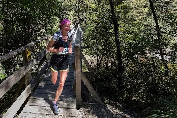 A woman is running across a wooden bridge in the woods.