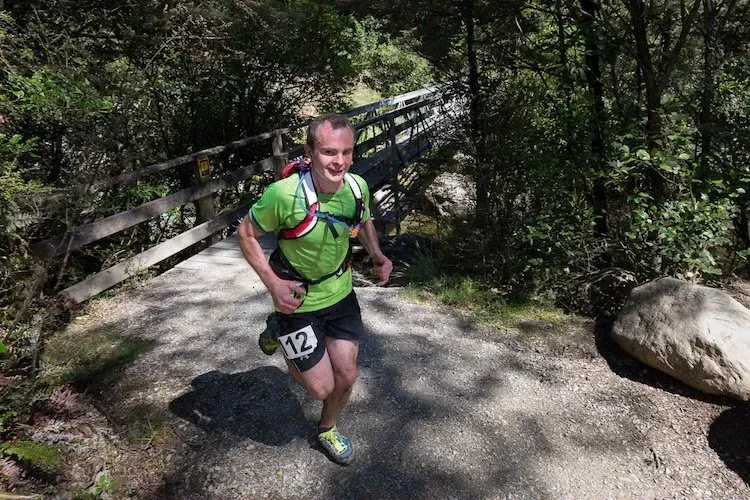 A man is running across a bridge in the woods.
