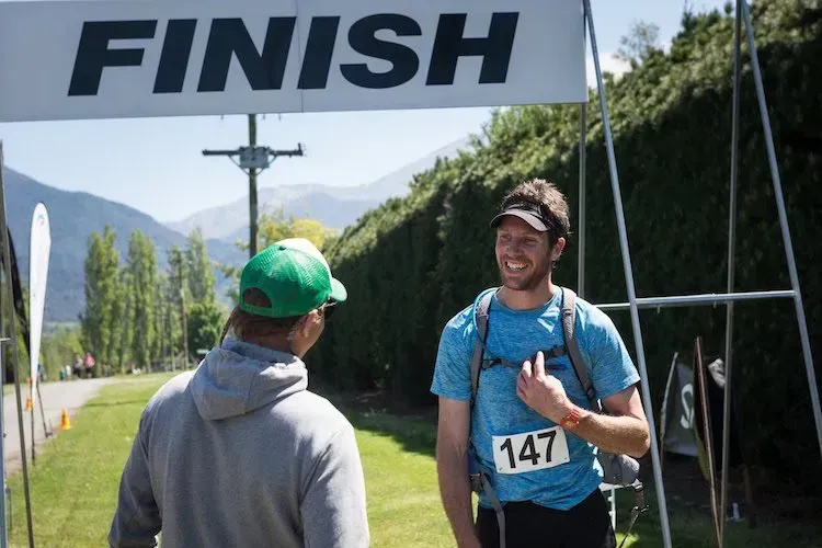 Two men are standing in front of a finish sign talking to each other.