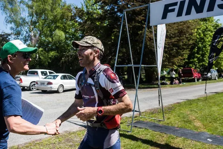 Two men are shaking hands at the finish line of a race.