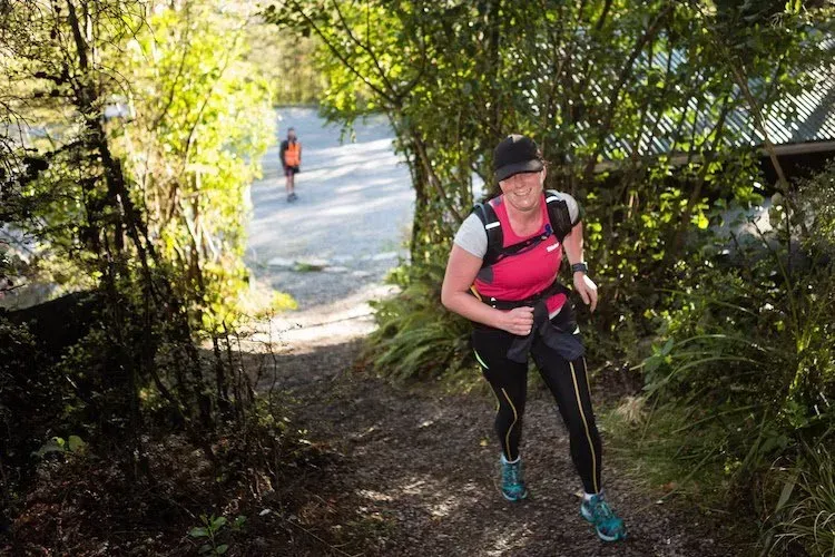 A woman is running down a trail in the woods.