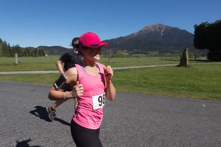 A woman in a pink tank top with the number 98 on it is running a race.