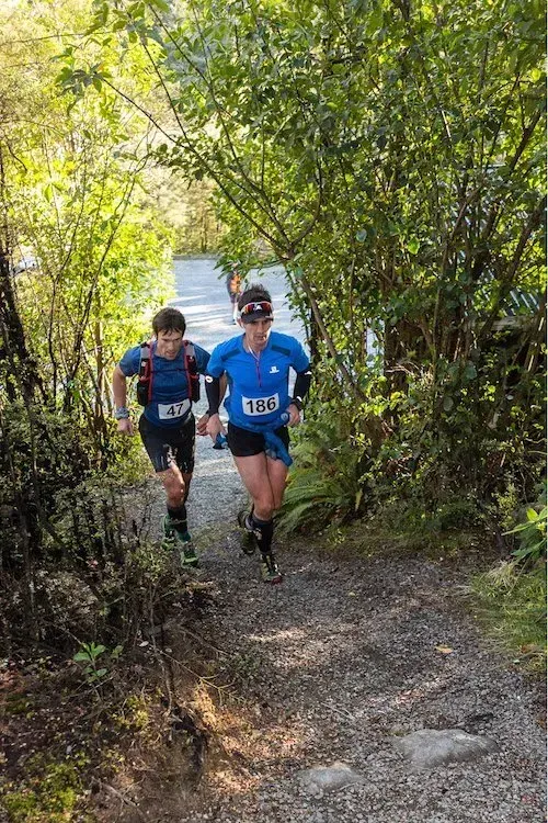 Two people are running down a path in the woods.