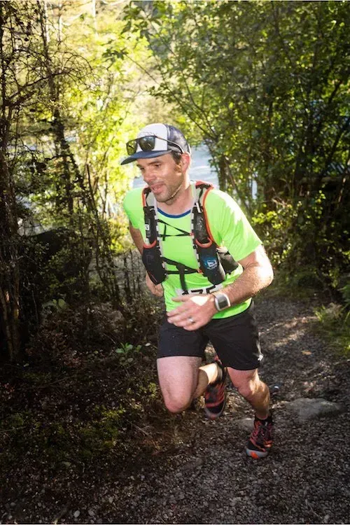 A man is running on a trail in the woods.