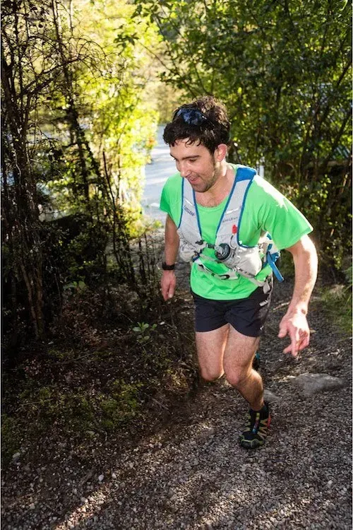 A man in a green shirt and black shorts is running down a trail.