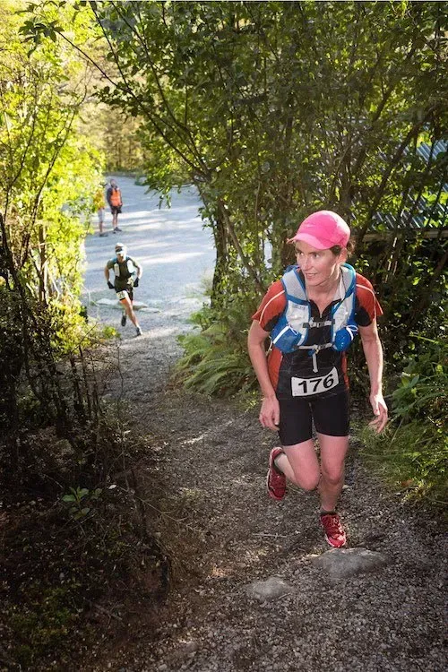 A woman is running up a trail in the woods.