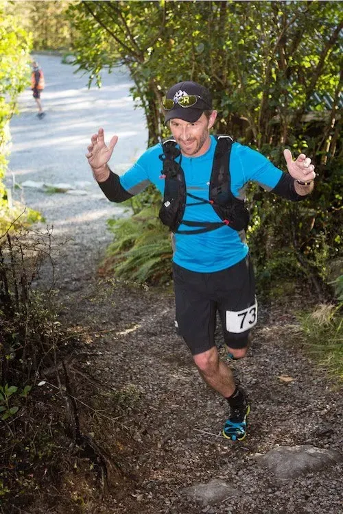 A man in a blue shirt and black shorts is running down a trail.