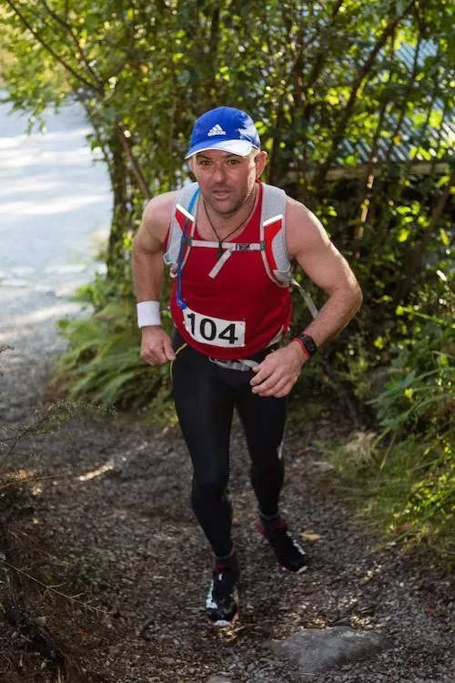A man wearing a red tank top with the number 104 on it is running up a hill.