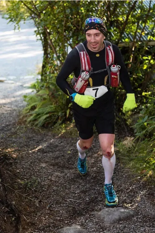 A man wearing a number 7 bib is running down a trail.