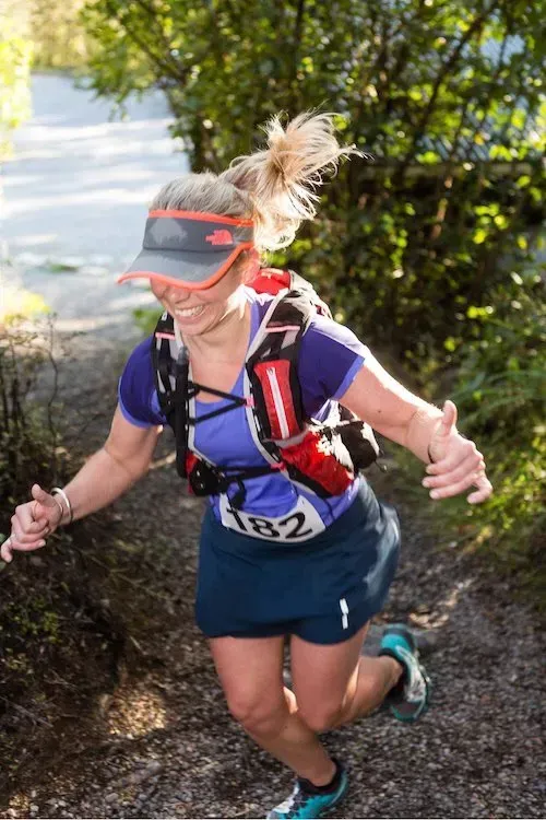 A woman is running down a trail with a water bottle in her hand.