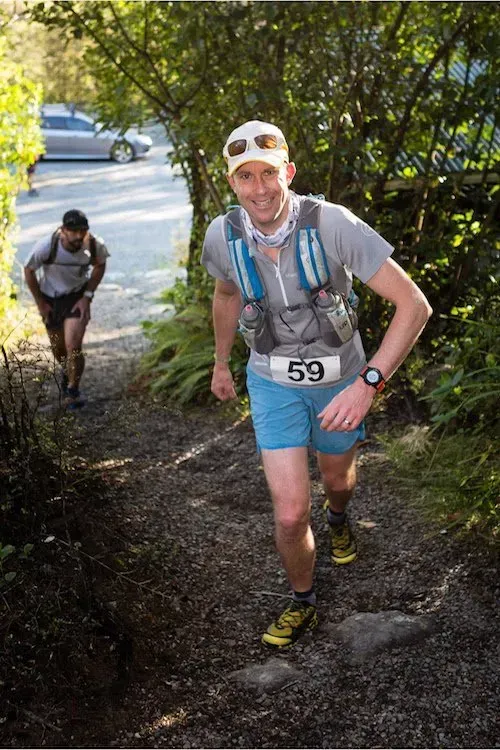 A man wearing a number 59 bib is running down a trail.
