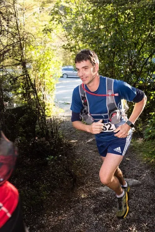 A man in a blue shirt and shorts is running down a trail.