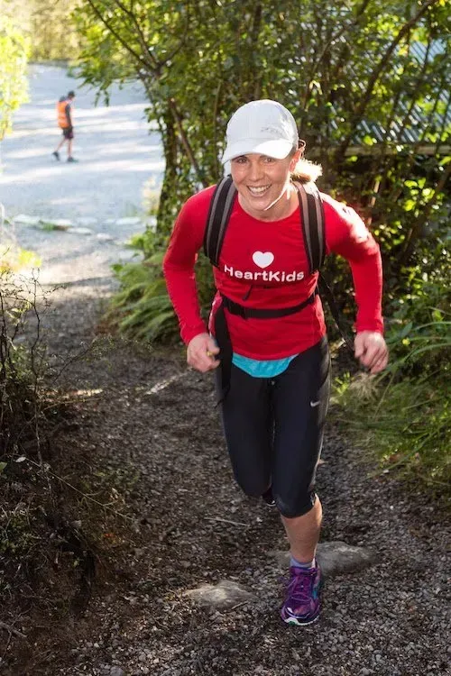 A woman wearing a red shirt that says heartkids is running down a path