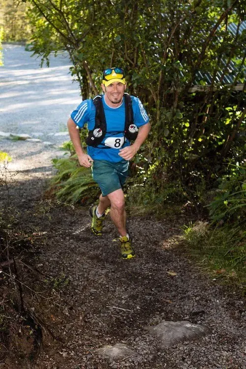 A man is running down a dirt path in the woods.