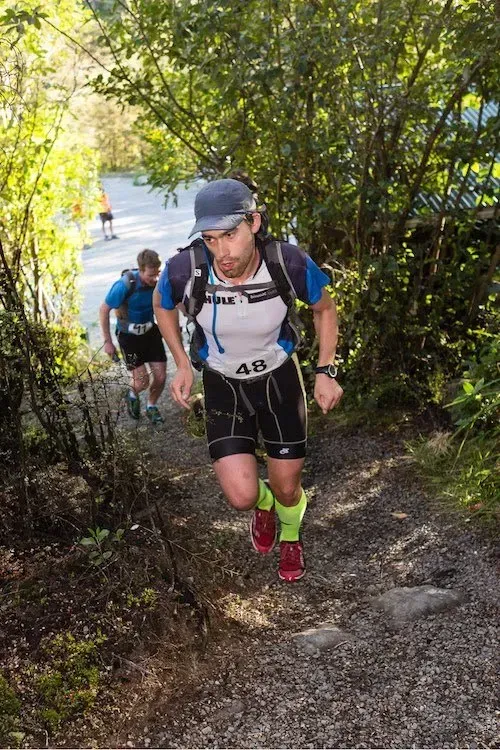 A man is running up a hill in the woods.