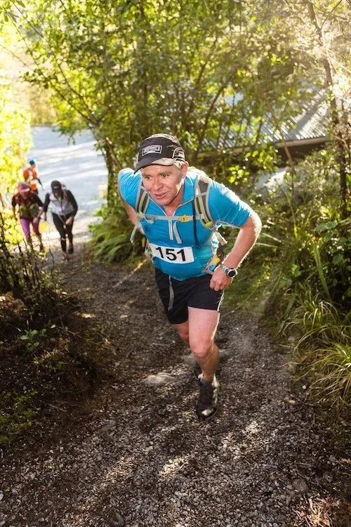 A man is running down a trail in the woods.