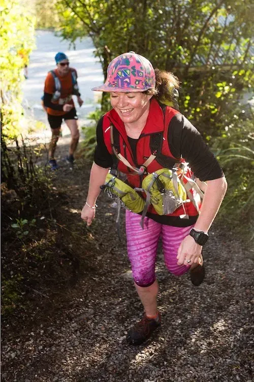 A woman is running down a trail with a backpack on her back.